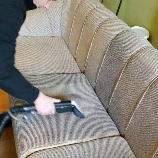 Pracovník tepuje sedák béžovej látkovej sedačky extrakčnou hubicou