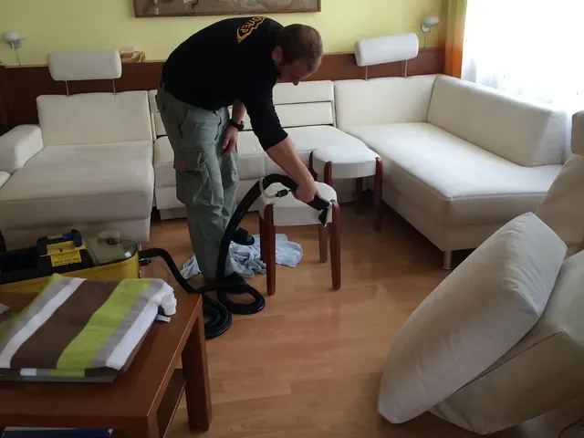 Pracovník firmy BODYTEP tepuje ručnou hubicou okrúhlu bielu taburetku v obývačke, v pozadí biela rohová sedačka